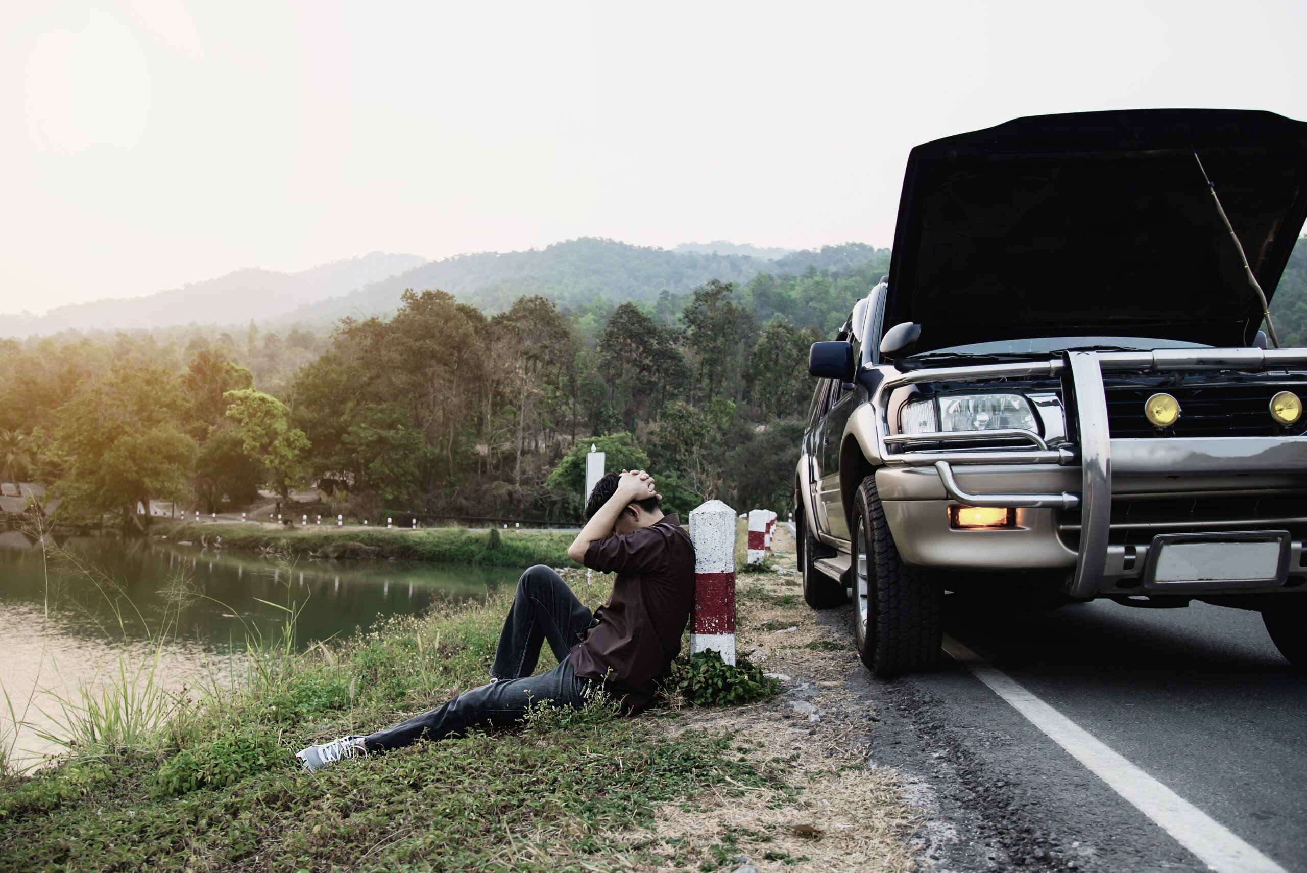 A man sits by a broken down car who needs towing services