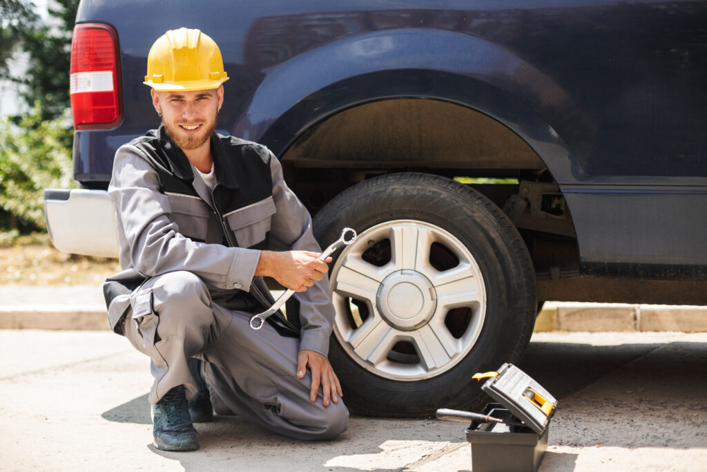 A man who works for a towing service sits next to a broken down car.